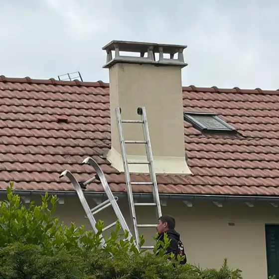 Couvreur CN Toiture à l'échelle sur une toiture en tuiles, souche de cheminée et fenêtre de toit à contrôler